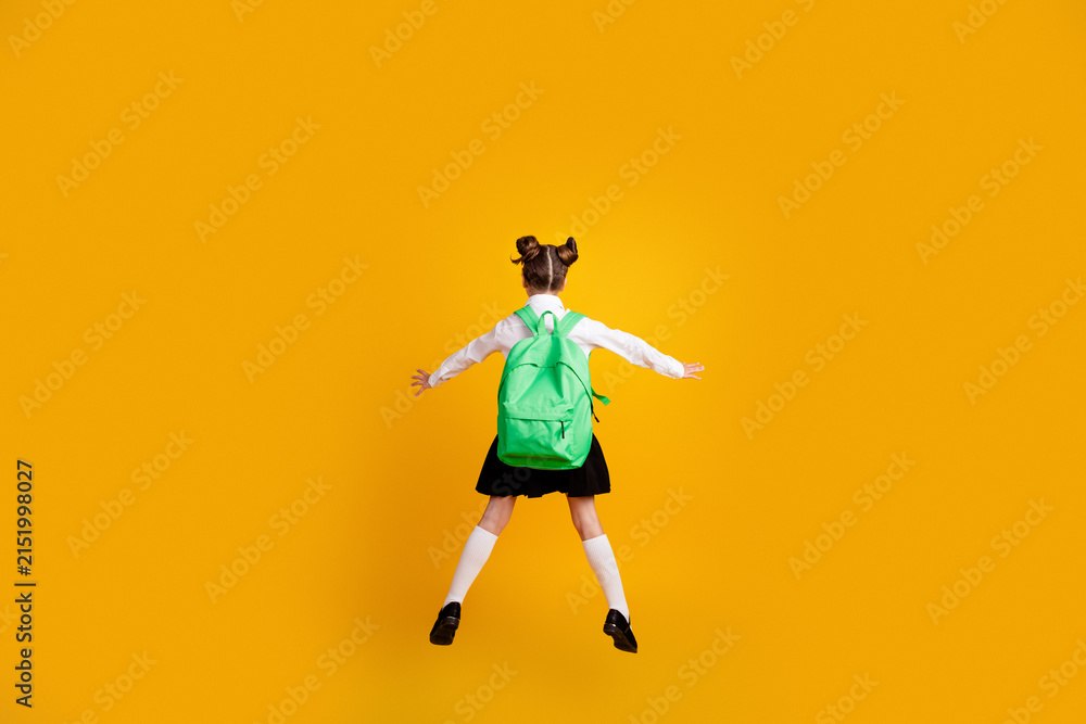 Obraz premium Excited schoolgirl jumping with green backpack on vibrant yellow background — back to school joy and playful childhood energy