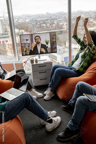 A diverse group of colleagues enjoys a successful video conference call while relaxing in beanbag chairs in a modern office space