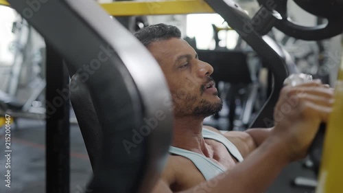 An Indian Asian fit healthy elderly or old man performs resistance or weight training exercise using a machine in a modern gym. Fitness, workout, healthy lifestyle, wellness. bodybuilding concept