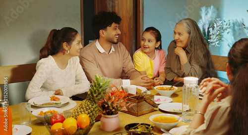 Indian happy relax joint family group sitting around table eat food talk speak share gossip have fun joy Young adult male female aged mom girl boy child spend time enjoy night dinner room home place