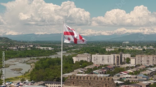 Georgian Flag Waving Over Gori Cityscape with Caucasus Mountains Background