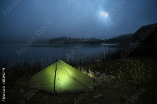 tent camping on Biviere lake in a foggy night landscape with a full moon, Nebrodi Park, Sicily, Italy 