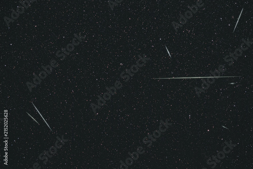 Meteors streak across a dense star field in the night sky.