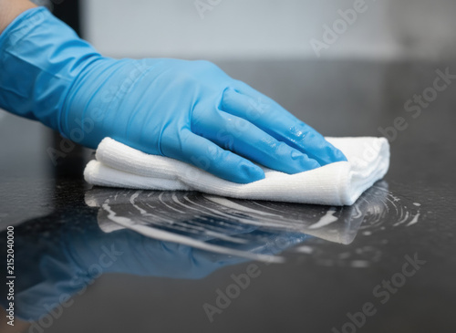 Hand in blue glove wiping down a dark surface with a white cloth
