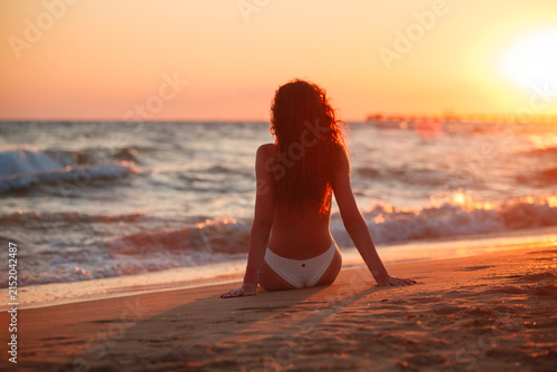 A girl is sitting with her back to the sea, watching the sunset, enjoying life style.