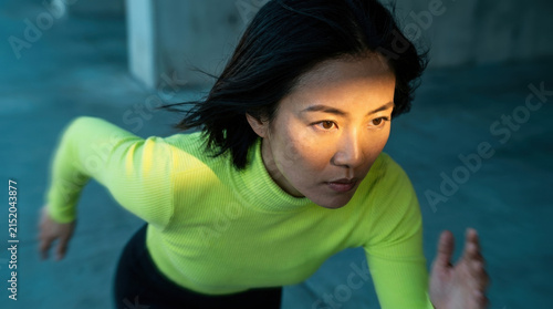 Determined Asian woman runner in neon top preparing for sprint