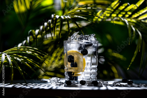 Blueberry lemonade mocktail with ice in a glass, on a table under sunlight. Fresh, tropical, and cold summer concept of a nonalcoholic drink.
