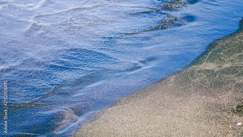 Konstfotografi Clear blue wave washing over dark sand on the beach shore.