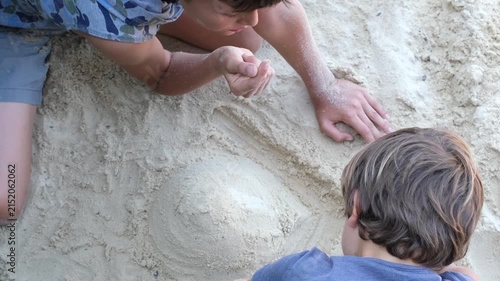 Two children work together to shape a sand volcano on white sand in an outdoor play area.