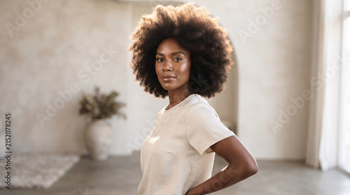 Portrait of a beautiful young woman with natural afro hair standing in a bright minimalist room.