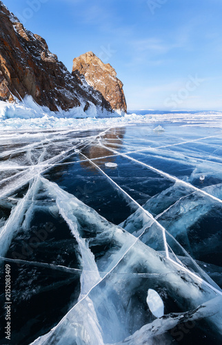 Scenic winter landscape of frozen Baikal Lake on February. View of famous natural landmark of Olkhon Island - Khoboy Cape or Deva Rock on background of blue sky. Winter travel and outdoor recreation