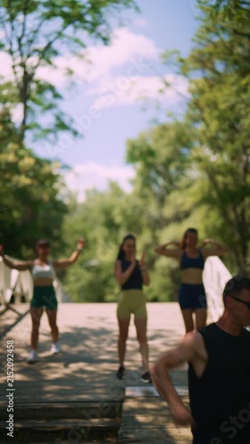 A group of active friends enjoys a fitness walk across a wooden bridge in a sunny park. They celebrate their strength and healthy lifestyle together outdoors.