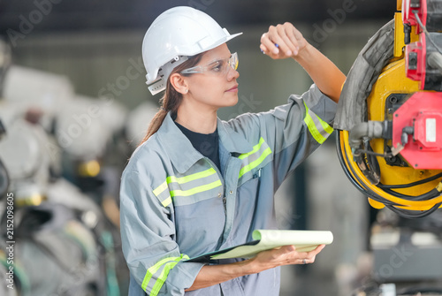 Female engineer in safety gear inspecting industrial machinery with a clipboard