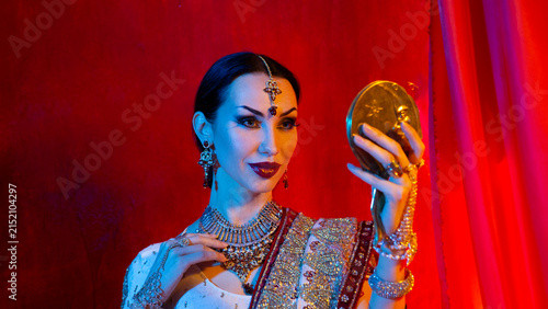 Woman in traditional Indian jewelry and sari holding a mirror