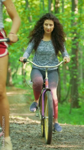 Walking on bicycles in the green forest two girls climb the path to the hill , sunny day