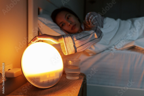 Photography Hand of asian woman pushing stop button on round-shaped light alarm clock with d