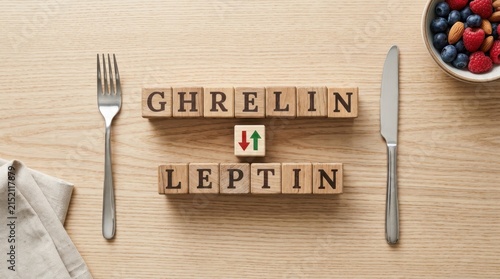 Wooden letter blocks spelling ghrelin and leptin hormones on dining table with cutlery and berries