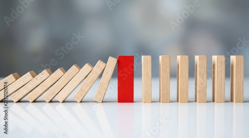 Red domino block stopping a chain reaction of falling wooden pieces on a table.