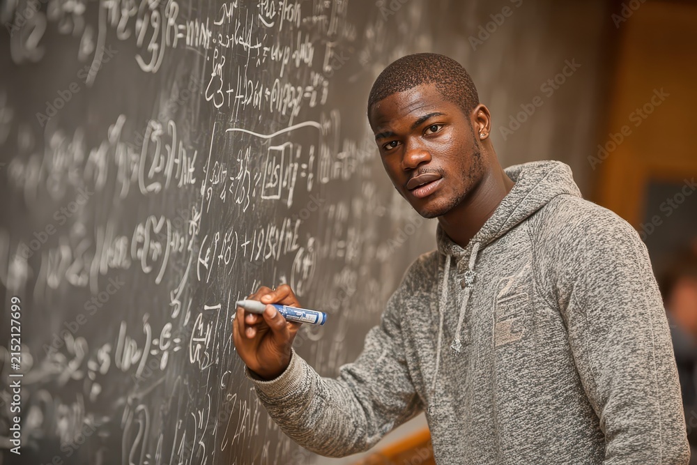 Fototapeta premium A student in a grey hoodie solves complex mathematical equations on the chalkboard, demonstrating his skill in math and commitment to education