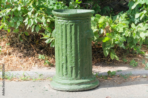 Cement trash can is painted green. Dumpster being for waste in a city park. Sunny day.