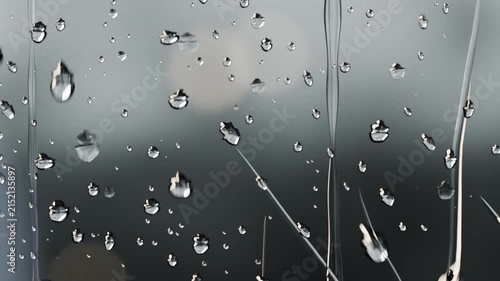 Sliding drops merging and streaming down vertical glass pane, rain causing coalescence and bokeh