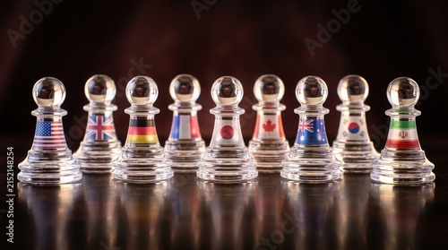 Glass chess pawns printed with international flags on a surface with standing reflective surface against dark background decorated international