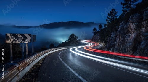 cinematic long exposure of car light trails on winding mountain road, misty valley view under starlit sky.