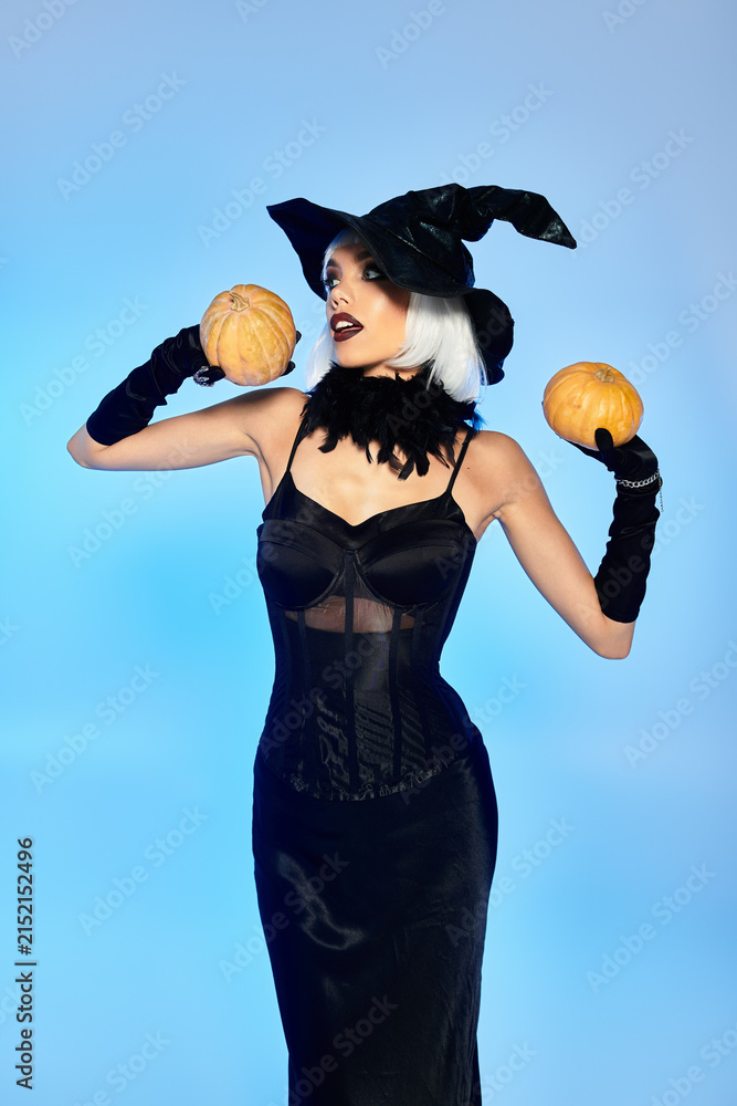 Obraz premium Glamorous witch in studio poses with pumpkins for a stylish Halloween look