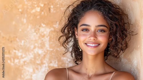 Smiling young woman with curly hair, natural beauty, warm expression, standing against textured wall, showcasing joy and confidence