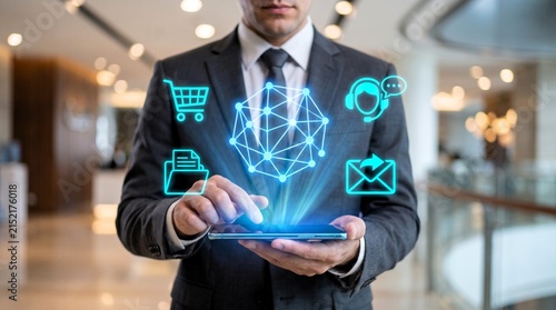 Professional businessman in dark suit interacts with glowing blue digital interface icons floating above his modern handheld mobile device screen
