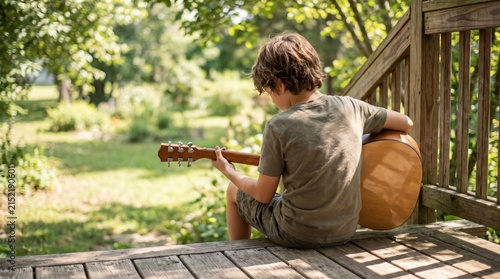 Boy Playing Acoustic Guitar on Porch Surrounded by Nature and Greenery