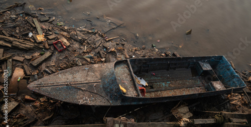 Fotografie Abandoned wooden fishing boat surrounded by waste