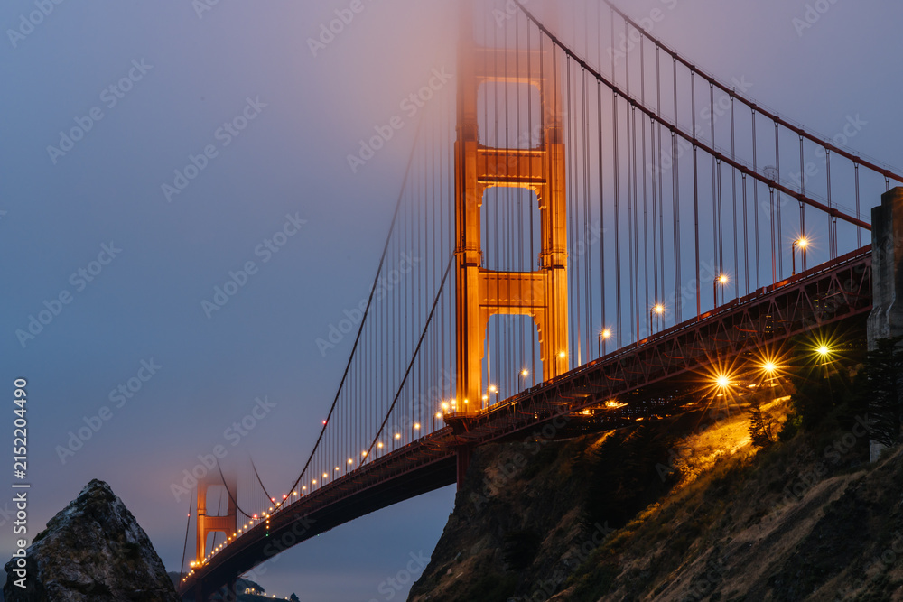 Naklejka premium Illuminated Golden Gate Bridge tower in San Francisco Bay fog seen from Fort Baker