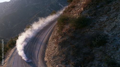 Aerial perspective of a car skillfully drifting along a twisting mountain road embraced by vibrant green foliage