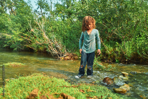 Boy standing in a shallow river looking down at the water