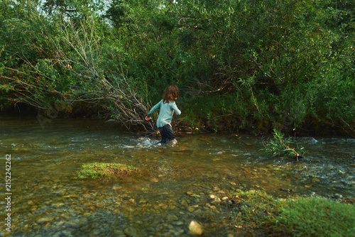 Boy wading alone in a river toward the far bank