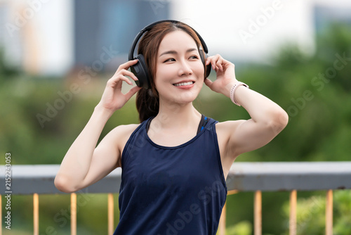Beautiful Asian woman relaxing after an outdoor workout in the evening, wearing wireless earbuds. Healthy lifestyle, fitness, wellness, beauty, and active living concept.