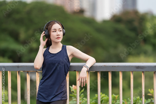 Beautiful Asian woman relaxing after an outdoor workout in the evening, wearing wireless earbuds. Healthy lifestyle, fitness, wellness, beauty, and active living concept.