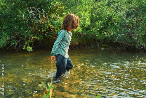 Boy wading knee-deep in a river in jeans and a sweater