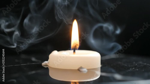 Burning tealight candle on black marble surface with smoke