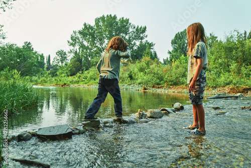 Two boys crossing a shallow river on stepping stones