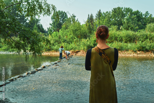Woman watching children play at a river from behind