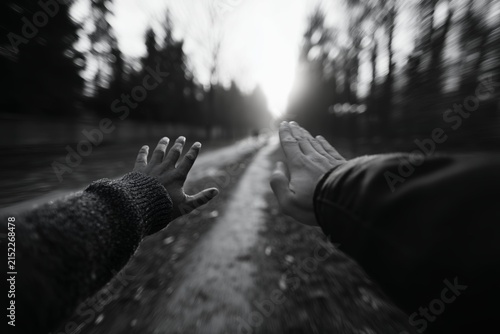 First person perspective hands reaching out on a blurred forest path towards a bright distant light symbolizing hope and journey.