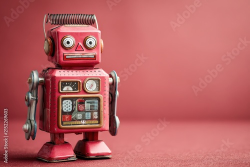 Vintage red tin robot toy with mechanical arms and clock face, standing against a solid pink background, showcasing retro design and nostalgic appeal