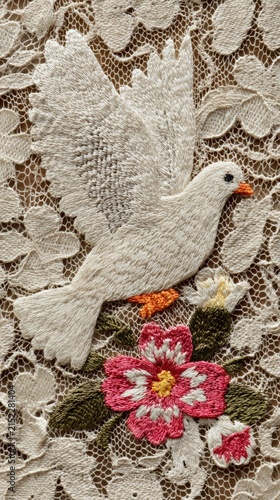 Embroidered white dove flying over colorful flower on vintage lace fabric. Detailed needlework bird and floral motif. Religious peace symbol and handmade textile craft decoration.