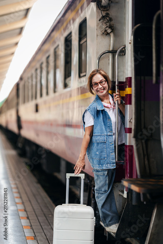 Foto Asian older woman joyful smile travels train with luggage at bustling railway st