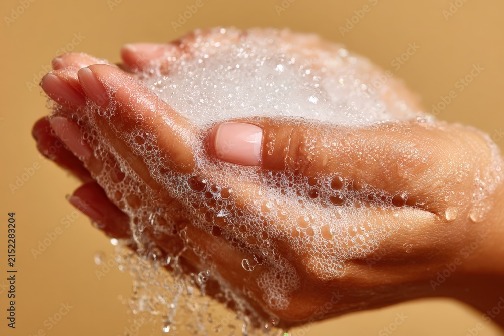 Fototapeta premium Close-up of female hands holding soap bubbles with a soft focus background, showcasing cleanliness and hygiene in a warm, neutral-toned setting