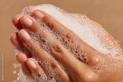 Close-up of hands with soap bubbles, showcasing a gentle washing motion against a soft, neutral background emphasizing cleanliness and hygiene practices