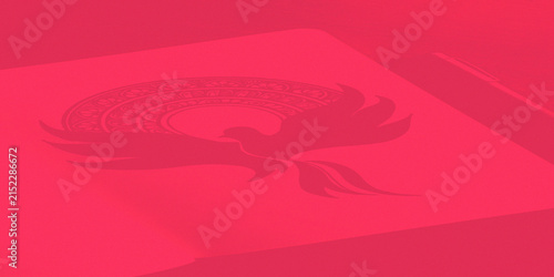 Red notebook with phoenix bird mandala drawing and pen a top view.