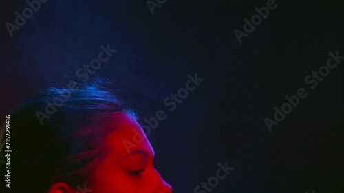 Close view of young beauty woman illuminated with red spraying fragrance and inhales the aroma on black background | Sensual beauty footage